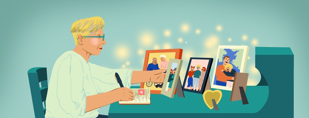 A middle-aged woman pauses writing in a journal at a desk to look at one of the many framed photos of a loved one with Alzheimer’s on the desk.