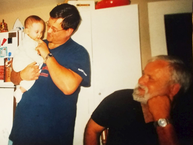 Amy's dad looking happily at his granddaughter who is being held by her father