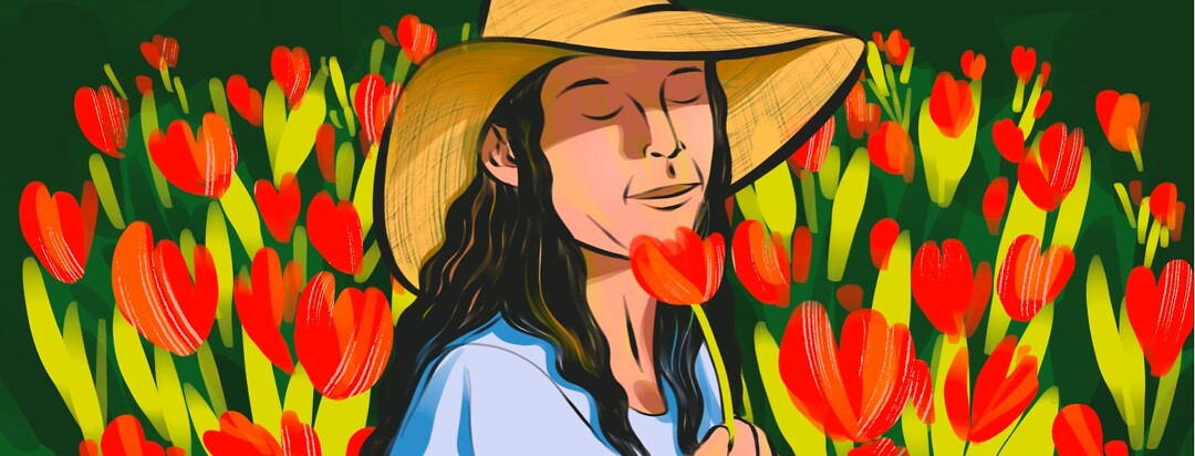 alt=A woman in a sunhat closes her eyes and smells a flower she is holding, while standing in a field of red flowers